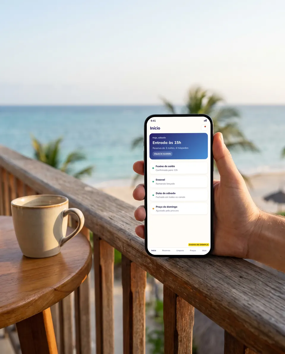 Mão segurando o celular numa varanda com o mar ao fundo, de manhã, com o app do apartamento na tela, dados de exemplo
